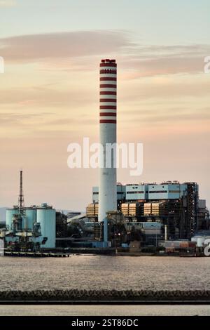 Grande centrale elettrica costiera con più camini a strisce vicino al mare, parte di un complesso industriale per la produzione e la distribuzione di energia. Concetto: Foto Stock