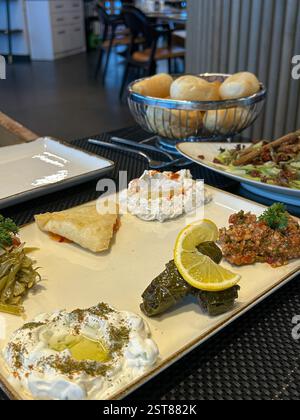 Questa elegante sala da pranzo presenta un piatto di antipasti mediterranei splendidamente organizzato con foglie d'uva ripiene con limone e tzatziki cremoso Foto Stock