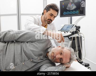 Il sonografo esamina il cervello di un uomo anziano posizionando il trasduttore a ultrasuoni sulla tempia della testa del paziente. Ecografia cranica con macchina a ultrasuoni Foto Stock