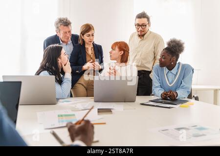 Team diversificato di professionisti che collaborano in un ufficio moderno, discutendo idee e strategie aziendali durante una riunione. Concetto di lavoro di squadra, leader Foto Stock