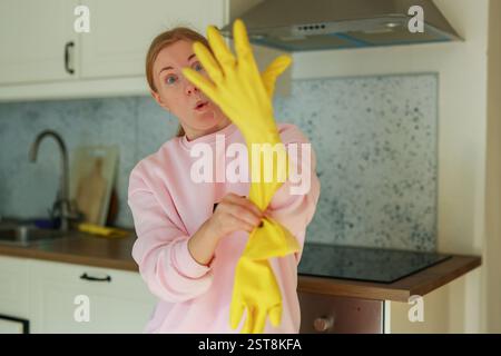 la ragazza indossa guanti di gomma gialli prima di pulire la casa Foto Stock