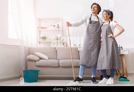 Professionisti della pulizia. Coppia di pulitori in grembiuli in posa in casa interno Foto Stock