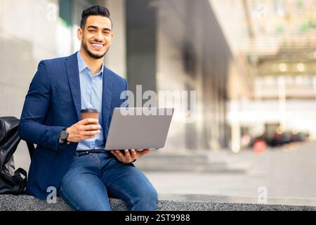 Un ragazzo medio-orientale positivo con un computer portatile che ha una pausa caffè all'aperto Foto Stock