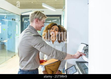 Due uomini d'affari che utilizzano una moderna stampante multifunzione in un ufficio di coworking, discutono del lavoro Foto Stock