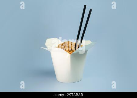 Wok spaghetti Udon con pollo in una scatola su sfondo blu. Con bacchette e salsa. Cibo asiatico da asporto Foto Stock