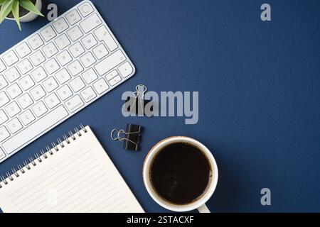 Spazio di lavoro con tastiera, forniture per ufficio, penna e tazza da caffè. Scrivania da ufficio blu con vista dall'alto Foto Stock