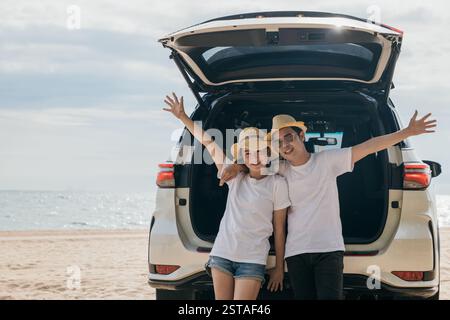 Una coppia asiatica sta posato sul retro di un'auto e gode di una splendida vista sulla spiaggia dell'oceano. uomo di stile di vita Foto Stock