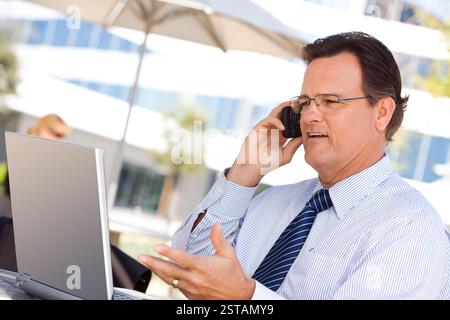 Bel uomo d'affari che parla al suo cellulare e lavora al portatile all'aperto. Foto Stock
