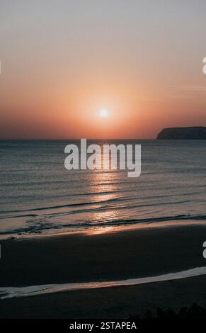 Il sole tramonta sull'oceano, proiettando un caldo bagliore sull'acqua. Il cielo è un mix di sfumature rosa e arancio che crea un'atmosfera serena e tranquilla Foto Stock