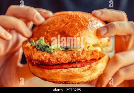 L'uomo tiene in mano l'hamburger con carne, formaggio e verdure. L'uomo tiene l'hamburger con le mani. Hamburger a mano, da vicino Foto Stock
