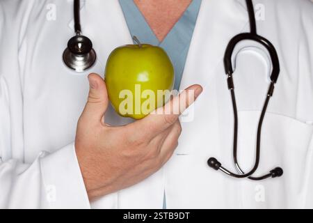 Medico maschio con stetoscopio che tiene la mela verde. Foto Stock