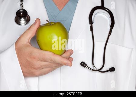 Medico maschio con stetoscopio che tiene la mela verde. Foto Stock