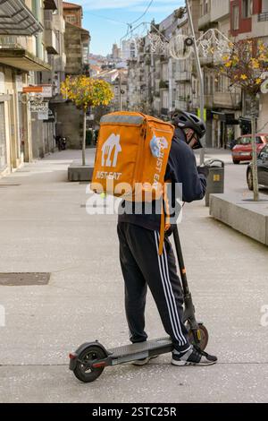 Vigo, Spagna - 14 gennaio 2025: Addetto alla consegna con uno scooter elettrico che lavora per Just Eat che controlla il suo telefono Foto Stock
