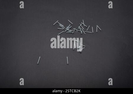 Piccole viti metalliche sparse in modo casuale su uno sfondo nero Foto Stock