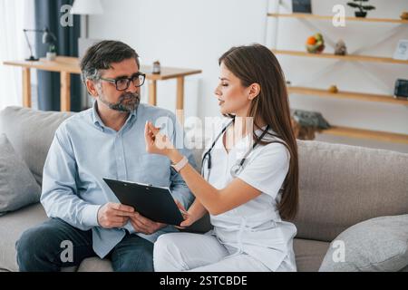 Lavorare con un uomo maturo. L'infermiera professionale è in ufficio con il mantello bianco. Foto Stock