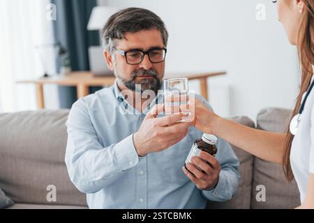 Dando le pillole e un bicchiere d'acqua. Operatore medico professionale in cappotto bianco è in ufficio. Foto Stock