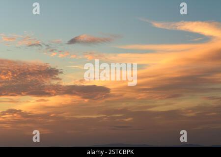 Una pittoresca scena al tramonto con nuvole sparse in tutto il cielo, che riflettono calde sfumature di arancione e giallo su un corpo d'acqua. Perfetto per i temi di Foto Stock