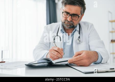 L'uomo sta lavorando con i documenti. Un medico maturo in giacca bianca è in ufficio. Foto Stock