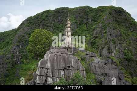 Pagoda tradizionale in pietra circondata da lussureggiante foresta verde e montagne rocciose presso l'Hang Mua a Ninh Binh Vietnam Foto Stock