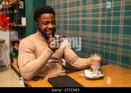 Il freelance si sta mettendo in pausa dal lavoro, sta parlando su smartphone e bevendo cioccolata calda al bar. Foto Stock