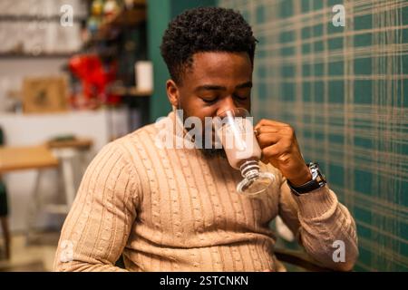 Giovane uomo di colore che si gusta la cioccolata calda al bar. Ritratto di un uomo che sta bevendo cioccolata calda. Foto Stock