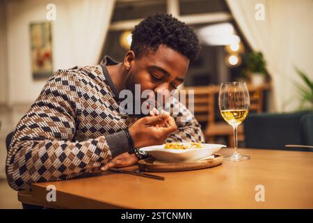Il giovane nero sta cenando e mangiando vino al ristorante. Foto Stock