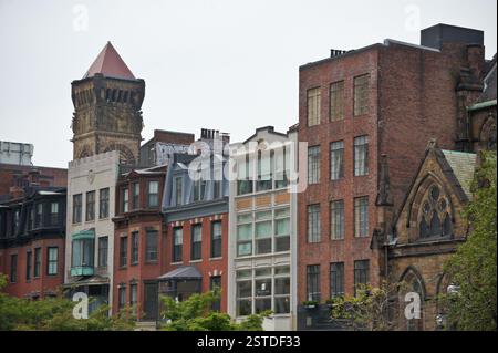 Boston: Una fila di colorati edifici in mattoni fiancheggiano la strada. Gli stili architettonici variano, dal classico al moderno. La torre si distingue contro lo Skylin Foto Stock