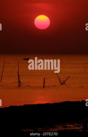 Un tramonto mozzafiato con vivaci tonalità di rosso e arancione che emettono un sereno bagliore sulle calme acque dell'oceano. L'orizzonte sagomato e il sole splendente creano una t Foto Stock