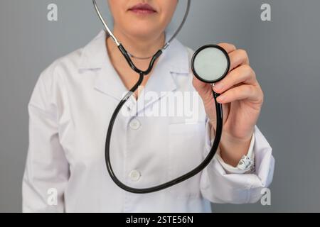 Anonimo operatore sanitario in un cappotto bianco tiene uno stetoscopio verso la fotocamera, simboleggiando l'esame e la cura medica Foto Stock
