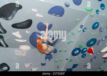 Una arrampicatrice affronta un percorso impegnativo su una parete interna di massi, mostrando forza e determinazione. Foto Stock