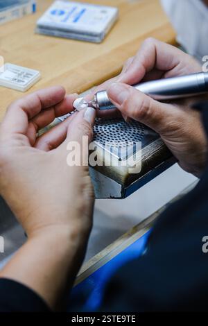 Dall'alto un primo piano irriconoscibile di mani che intagliano meticolosamente un piccolo oggetto con uno strumento rotante nello spazio di lavoro di un gioielliere, concentrato e detai Foto Stock