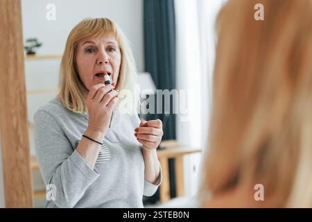 Guarda lo specchio, cura di sé. Una donna anziana con i capelli rossi è a casa da sola. Foto Stock