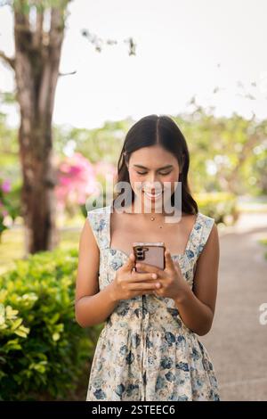 Giovane donna asiatica che scrive con il telefono all'aperto Foto Stock