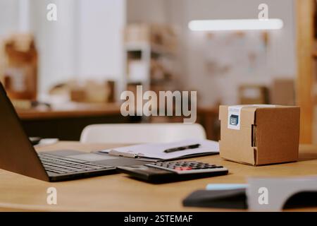 Moderna scrivania da ufficio con computer portatile, calcolatrice e scatola di cartone nell'area di lavoro organizzata con diverse forniture per ufficio e sfondo sfocato delle attrezzature per ufficio Foto Stock