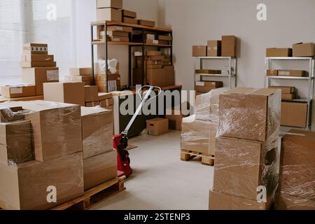 Una collezione di scatole di cartone marrone di varie dimensioni impilate su pallet e ripiani in legno in un ambiente di magazzino Foto Stock