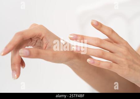 Bella donna asiatica che applica prodotti per la cura della pelle alla mano, mostrando bellezza e cura di sé in uno sfondo bianco Foto Stock