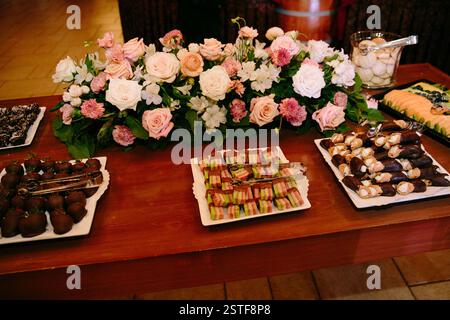 Un tavolo splendidamente organizzato che presenta dessert assortiti e vivaci decorazioni floreali per un incontro gioioso. Foto Stock