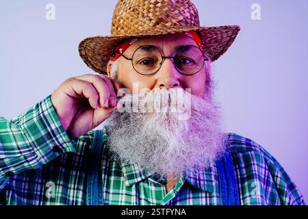 Vecchio anziano con barba grigia che indossa il ritratto dell'abito contadino in studio - divertente elegante lavoratore agricolo adulto con uno stile cool, concetti su Foto Stock