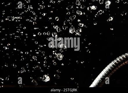 Gocce d'acqua levitano su uno sfondo scuro e su un tubo Foto Stock