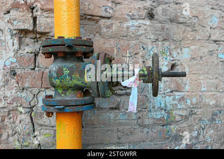 Vecchia tubazione gas dipinte di giallo tubo e valvola di ruggine con macchie di vernice obsoleti in corrispondenza di un muro di mattoni Foto Stock