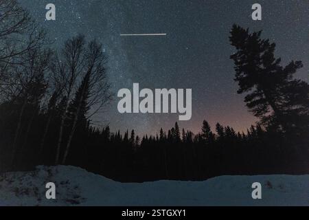 Un aereo a reazione perfora il cielo notturno con la via lattiginosa sullo sfondo in una fredda notte invernale vicino a Grand Marais Minnesota Foto Stock
