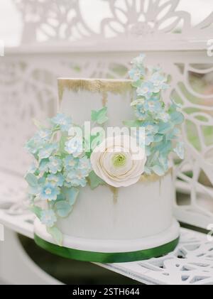 Una splendida torta nuziale adornata da delicati fiori pastello è esposta in un affascinante locale all'aperto. Foto Stock