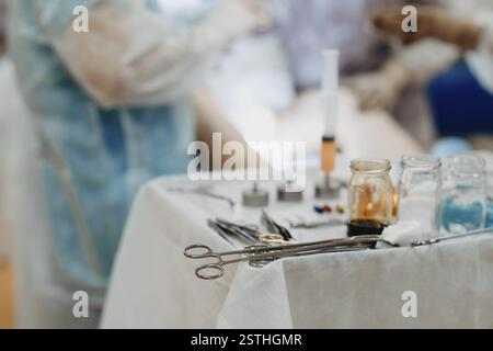 Una varietà di strumenti chirurgici e siringhe sono disposti su un tavolo medico durante una procedura Foto Stock