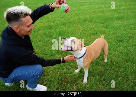 Giovane che gioca con il suo cane nel parco. L'uomo tiene giocosamente una palla sopra la bocca di un moggy. Amicizia tra cane e uomo. Foto Stock