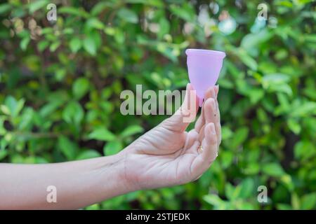 Vista ravvicinata di una donna che tiene la tazza mestruale su un vero sfondo naturale. Periodo femminile, concetto di coppa mestruale. Foto Stock