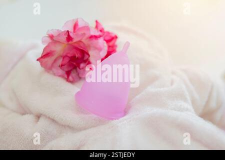 Coppetta mestruale rosa eco-compatibile, riutilizzabile, realizzata in morbido silicone per uso medico su asciugamano con fiore e spazio di copia. Foto Stock
