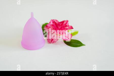 Tazza mestruale rosa con vista laterale fiori e foglie verdi. Salute delle donne, coppetta mestruale come concetto zero sprechi. Foto Stock