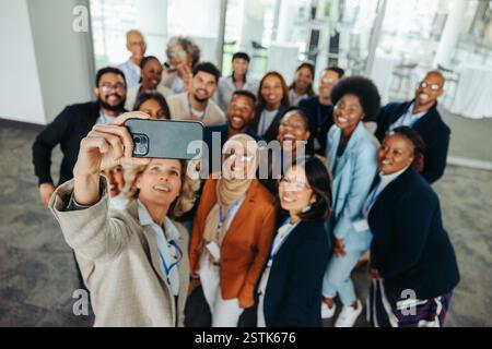 Gruppi diversificati di professionisti che sorridono e scattano un selfie insieme durante un evento aziendale. Opportunità di networking e Unione dei team. Foto Stock