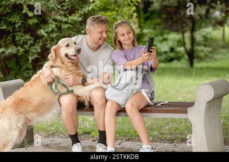Padre e figlia che portano Un divertente Selfie con Golden Retriever al parco Foto Stock