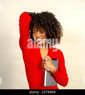 Ritratto in studio di una allegra donna d'affari in rosso che tiene in mano un tablet e si tocca i capelli Foto Stock